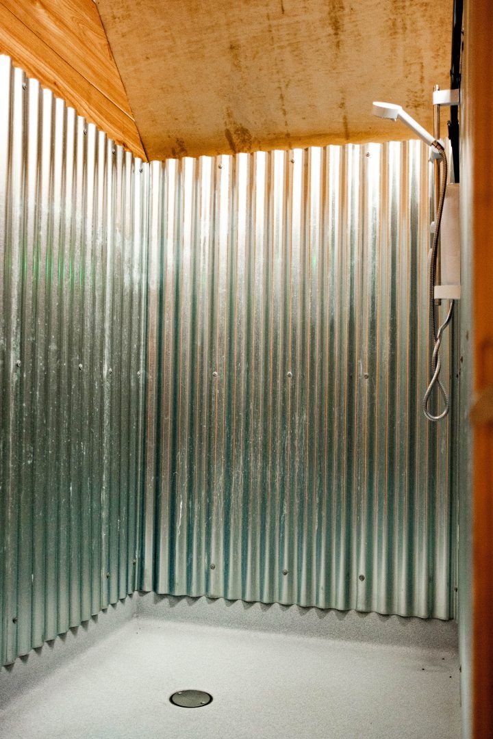 The shared shower cubicle with corrugated metal walls and a shower tray